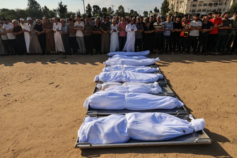 FOTO : Para pelayat mendoakan jenazah anggota keluarga Agha yang dikafani, pada 14 Oktober 2023 [Mahmud Hams/AFP]