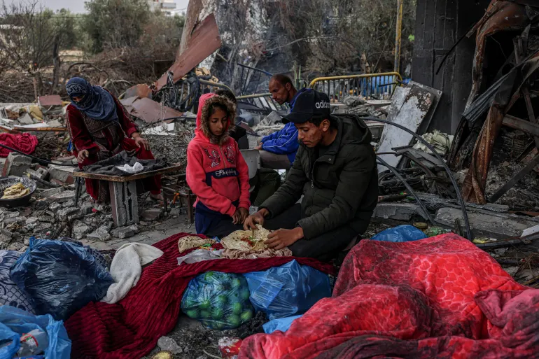 FOTO : Warga Palestina makan di luar, dikelilingi kehancuran akibat serangan udara Israel di desa Khuzaa, sebelah timur Khan Younis di selatan Jalur Gaza pada 27 November 2023 [Said Khatib/AFP]